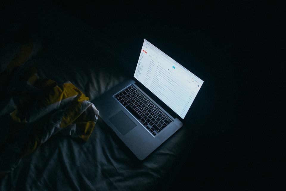Laptop open in a dark bedroom showing Gmail inbox, illustrating running out of G Suite storage