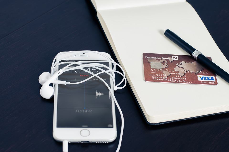 Smartphone with earphones beside a notebook and Visa card on a dark desk
