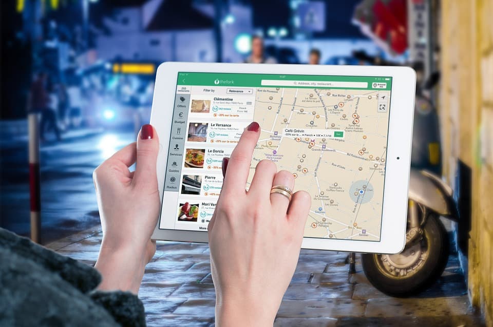 Person using a tablet to browse a restaurant finder app with a city map and listing results