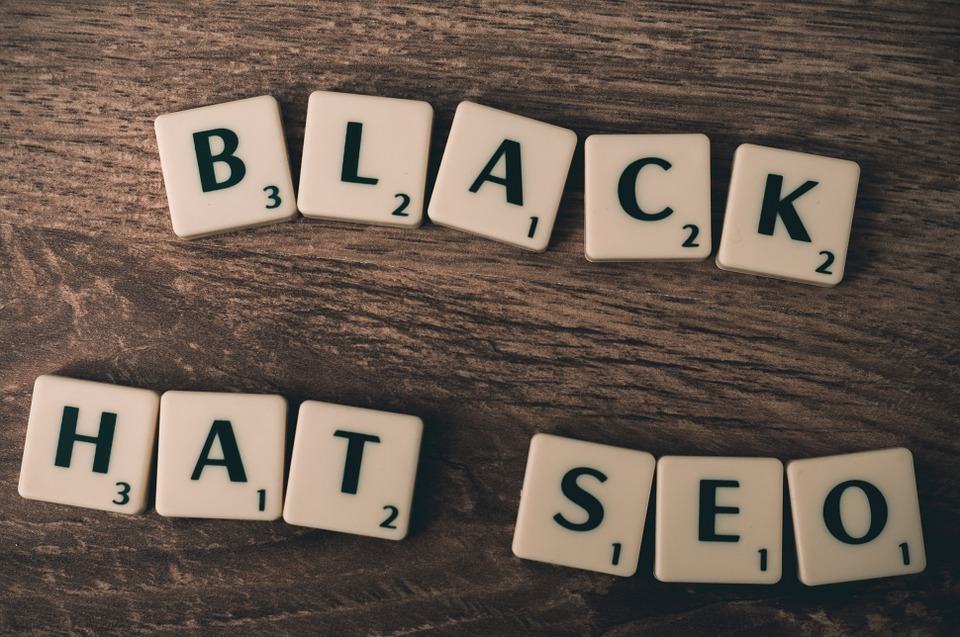 Scrabble tiles spelling Black Hat SEO on a wooden surface, illustrating prohibited SEO practices