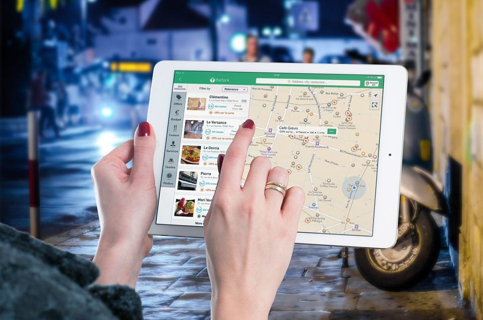 Woman holding a tablet showing a local restaurant map app with listings and directions, representing local SEO search