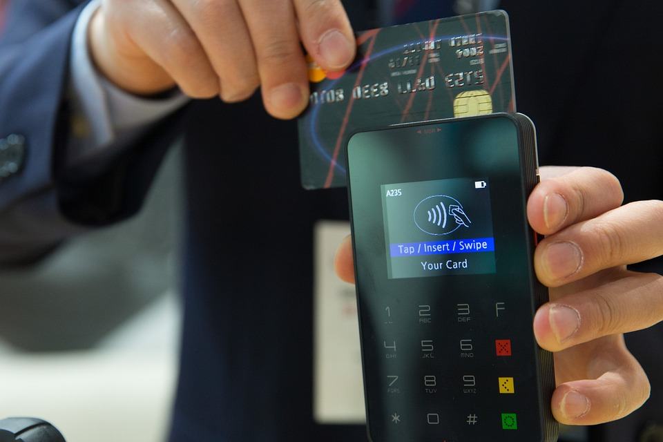 Person inserting a credit card into a contactless payment terminal showing Tap/Insert/Swipe prompt, illustrating ecommerce transactions