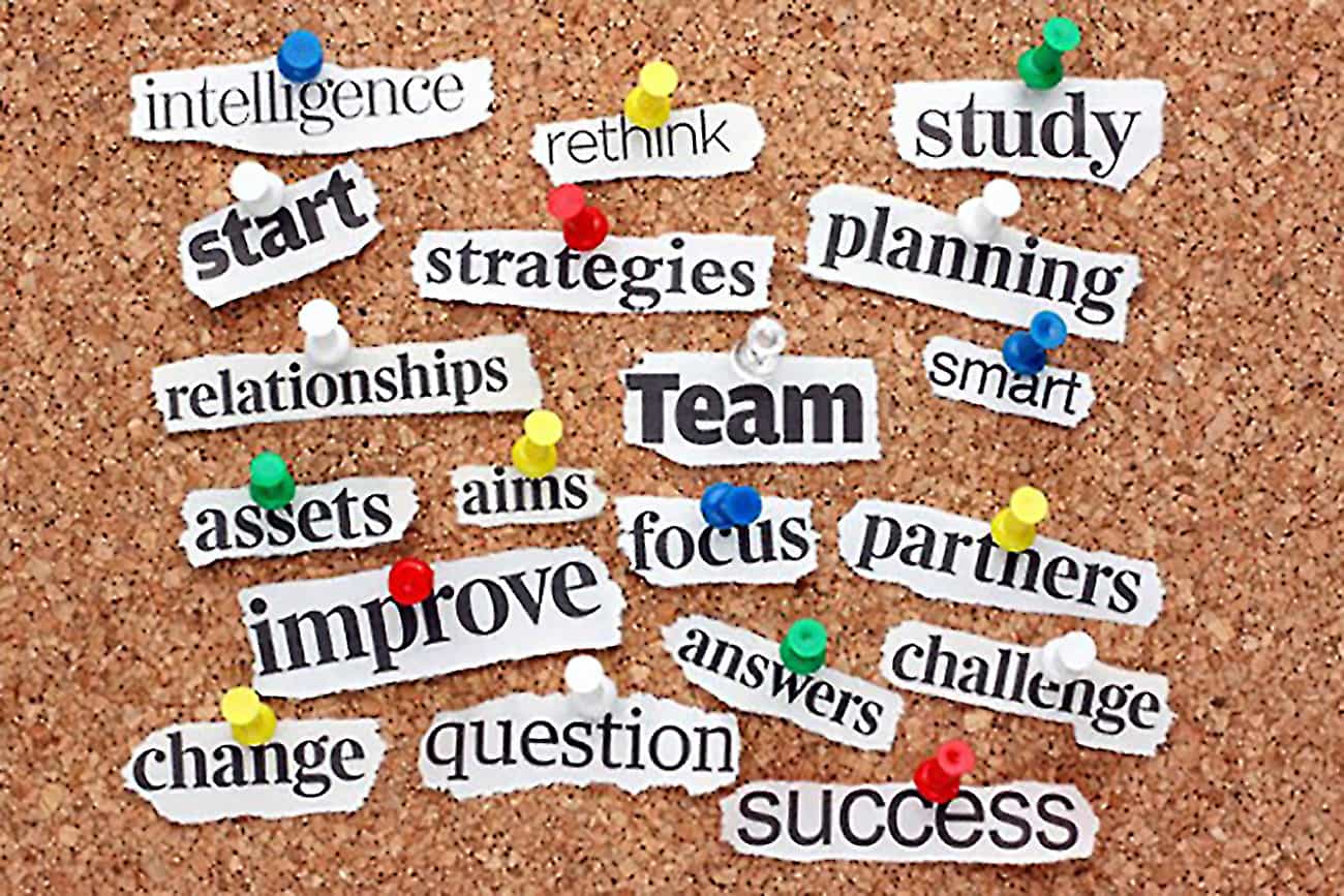 Strategy keywords including team, focus, improve and planning pinned on a cork noticeboard with colourful drawing pins