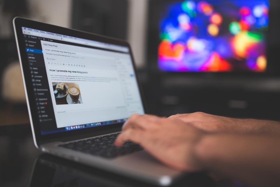 Person typing a WordPress blog post on a MacBook laptop with a colourful bokeh screen visible in the background