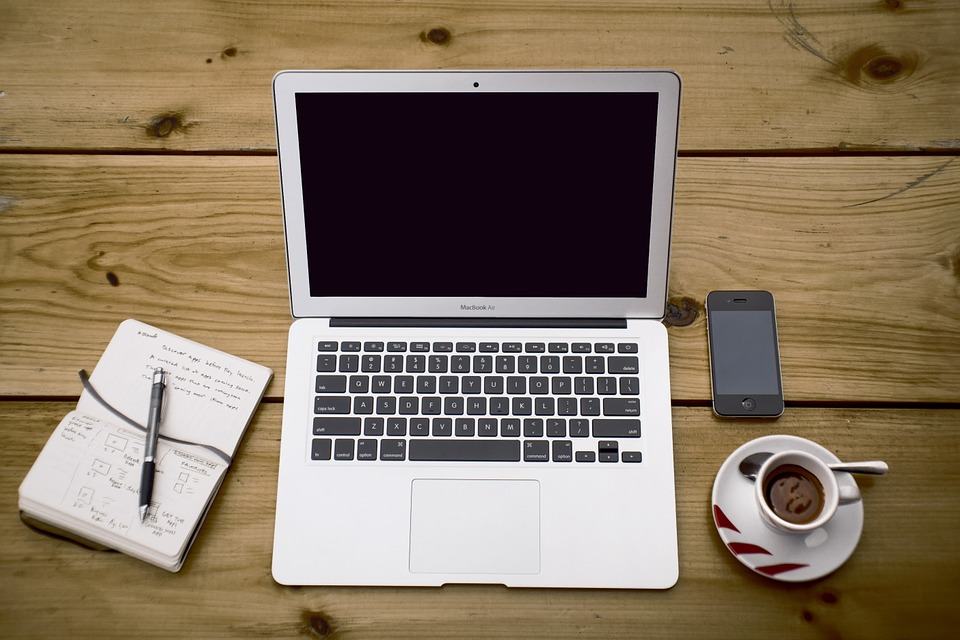 MacBook Air, notepad with wireframe sketches, smartphone and espresso cup arranged on a wooden desk