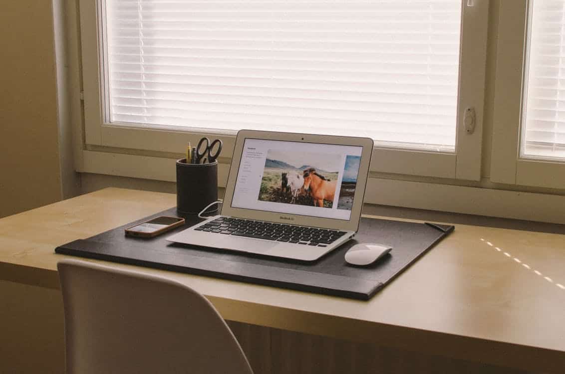 MacBook Air on a tidy desk showing a website with nature photography, beside a phone and pen pot