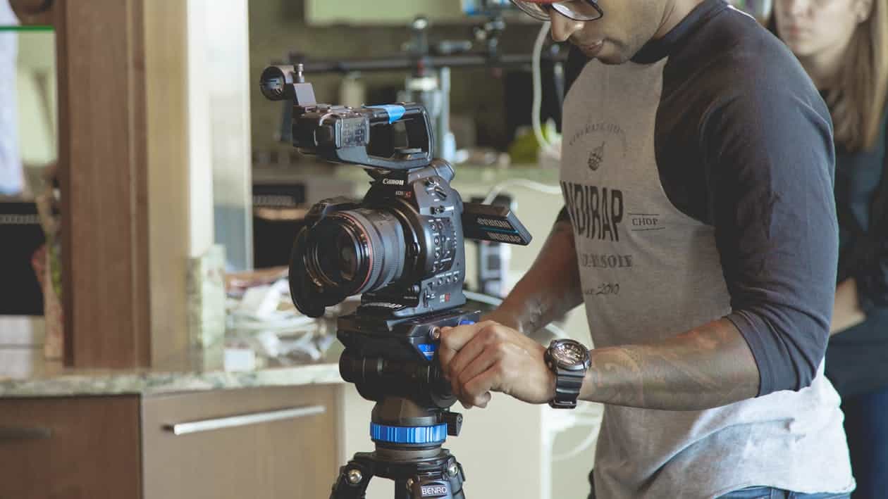 Videographer adjusting a Canon cinema camera on a Benro tripod, representing professional video content production