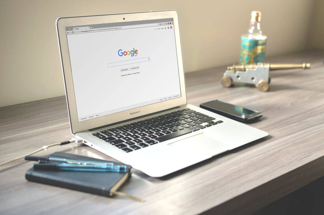 MacBook Air displaying the Google homepage on a wooden desk with a notebook and phone nearby