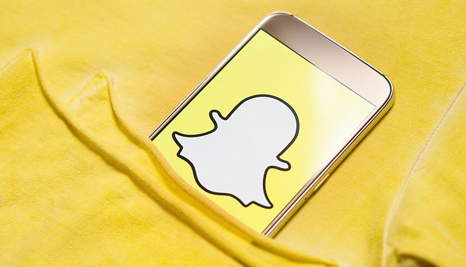 Snapchat ghost logo displayed on a smartphone screen resting in the pocket of a yellow T-shirt