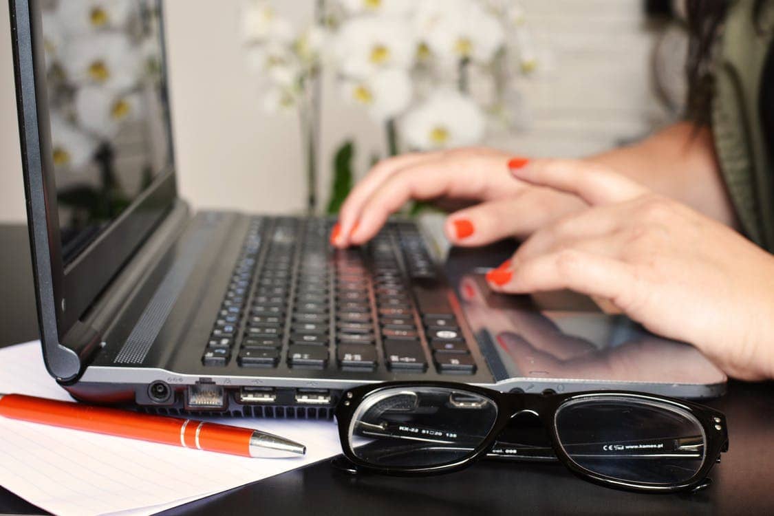 Woman typing on a laptop with glasses and a red pen resting in the foreground