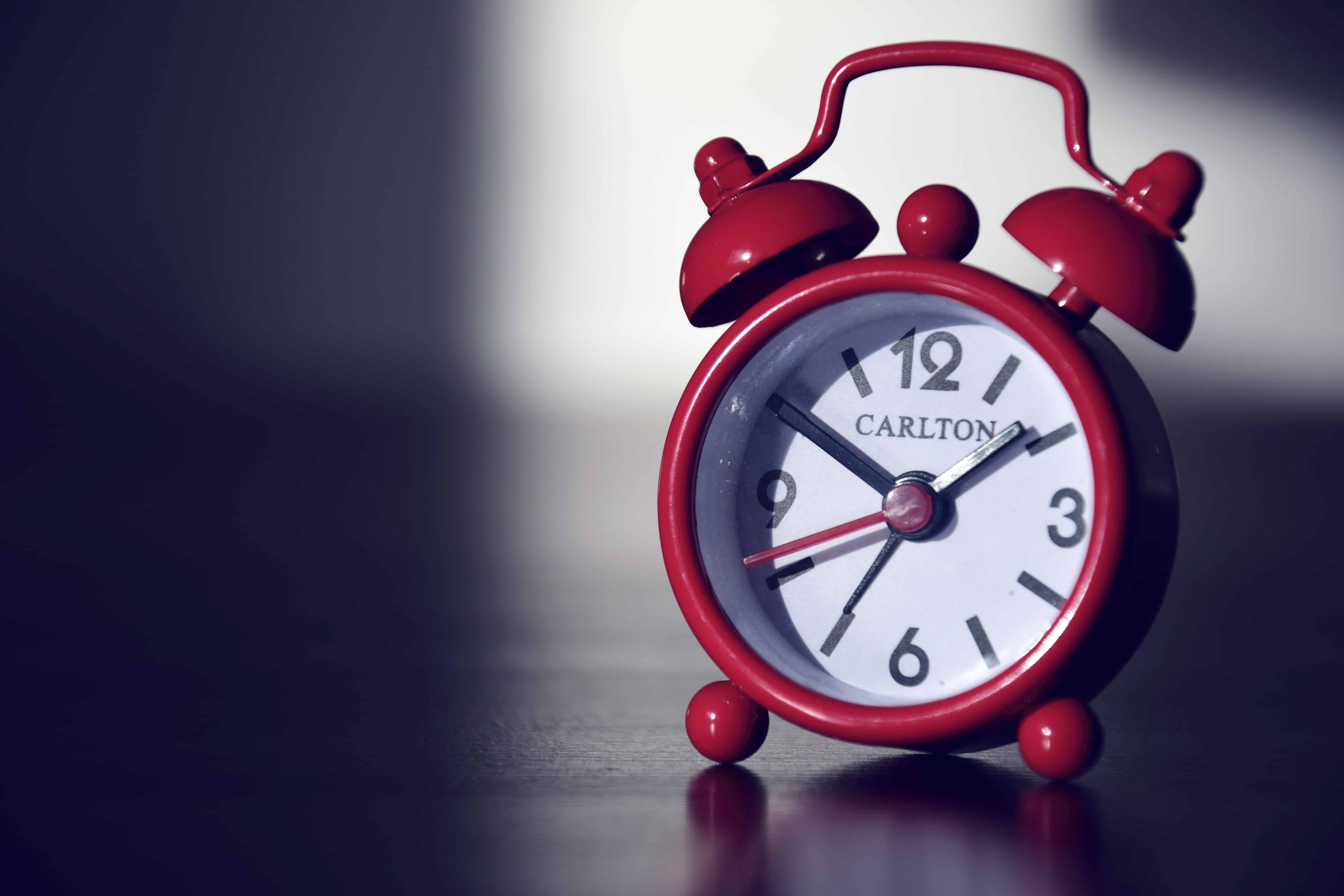 Red Carlton alarm clock on a dark surface representing time management productivity tips