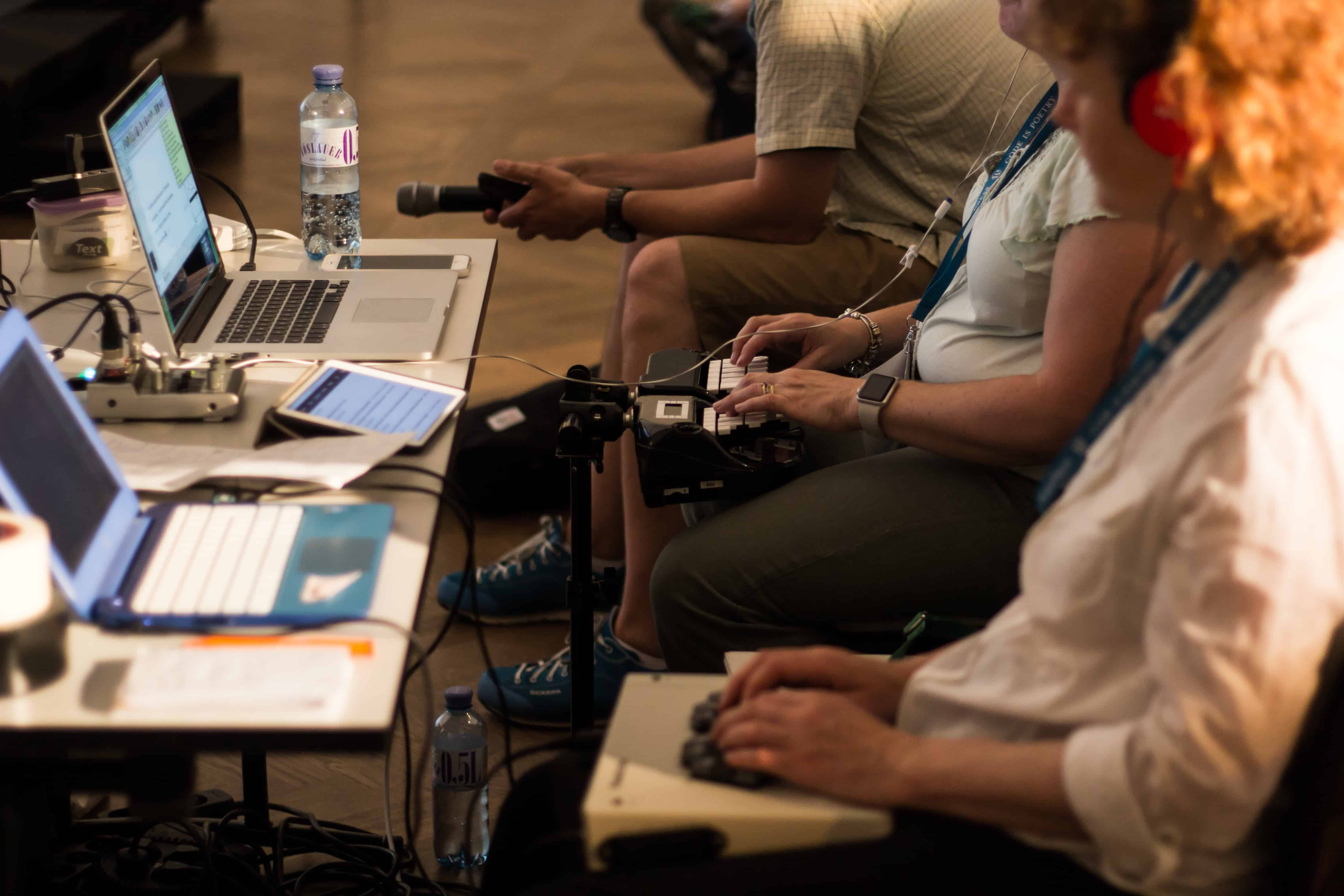 Conference attendees working on laptops and recording equipment at a technology event