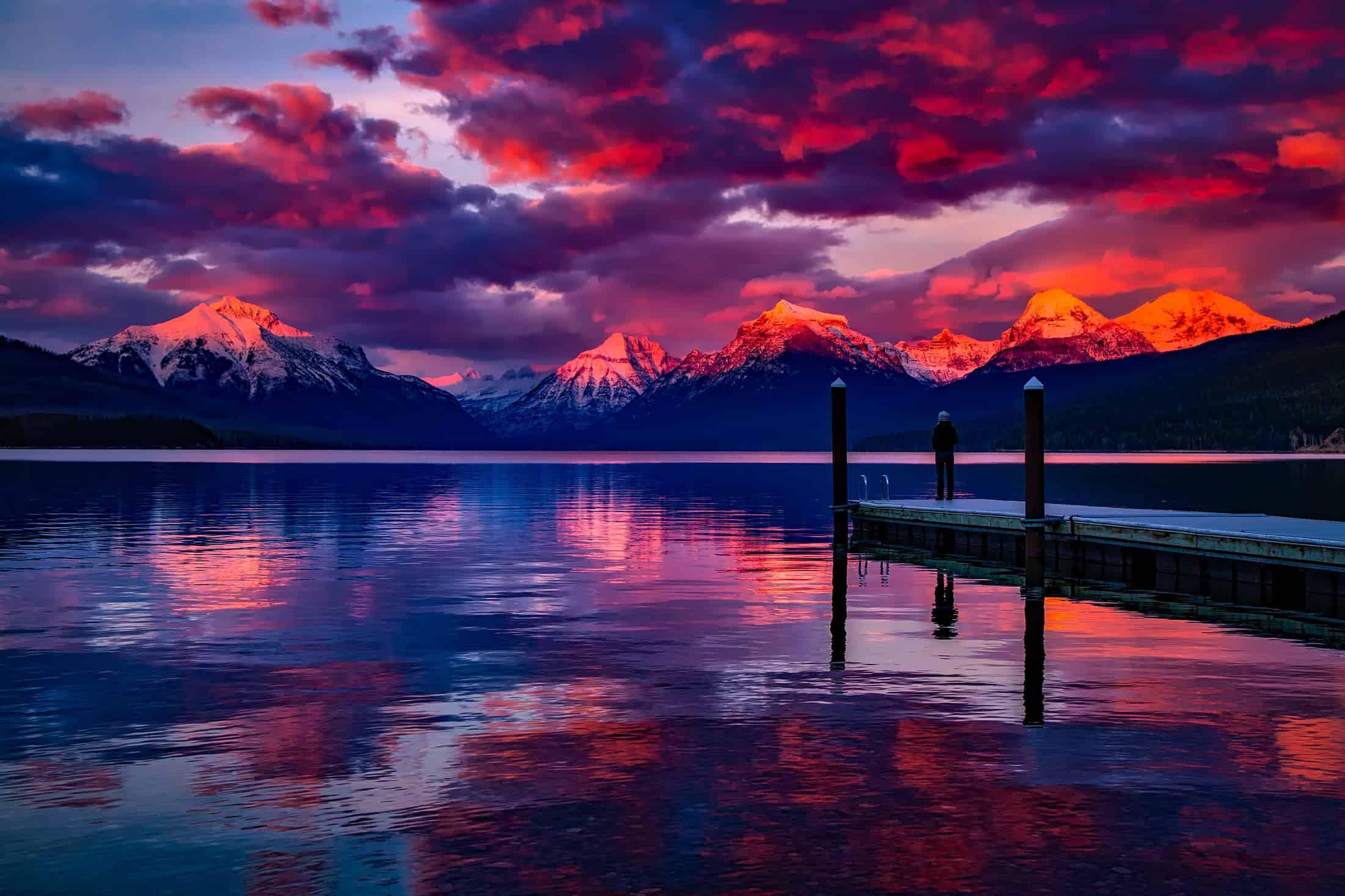 Dramatic sunset over a mountain lake with vivid pink and purple sky reflected in the water