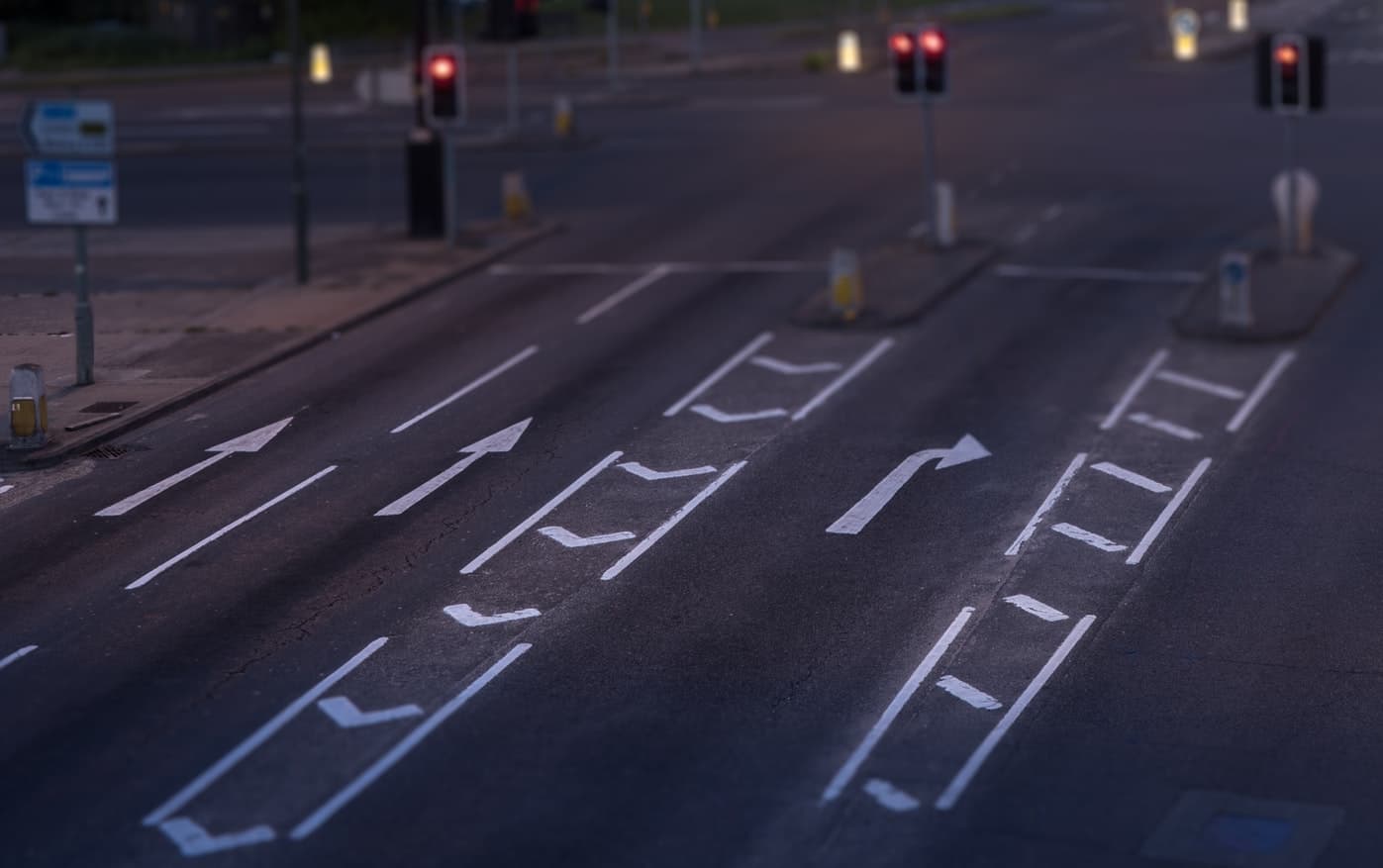 Multi-lane road junction at dusk with white directional arrows and red traffic lights