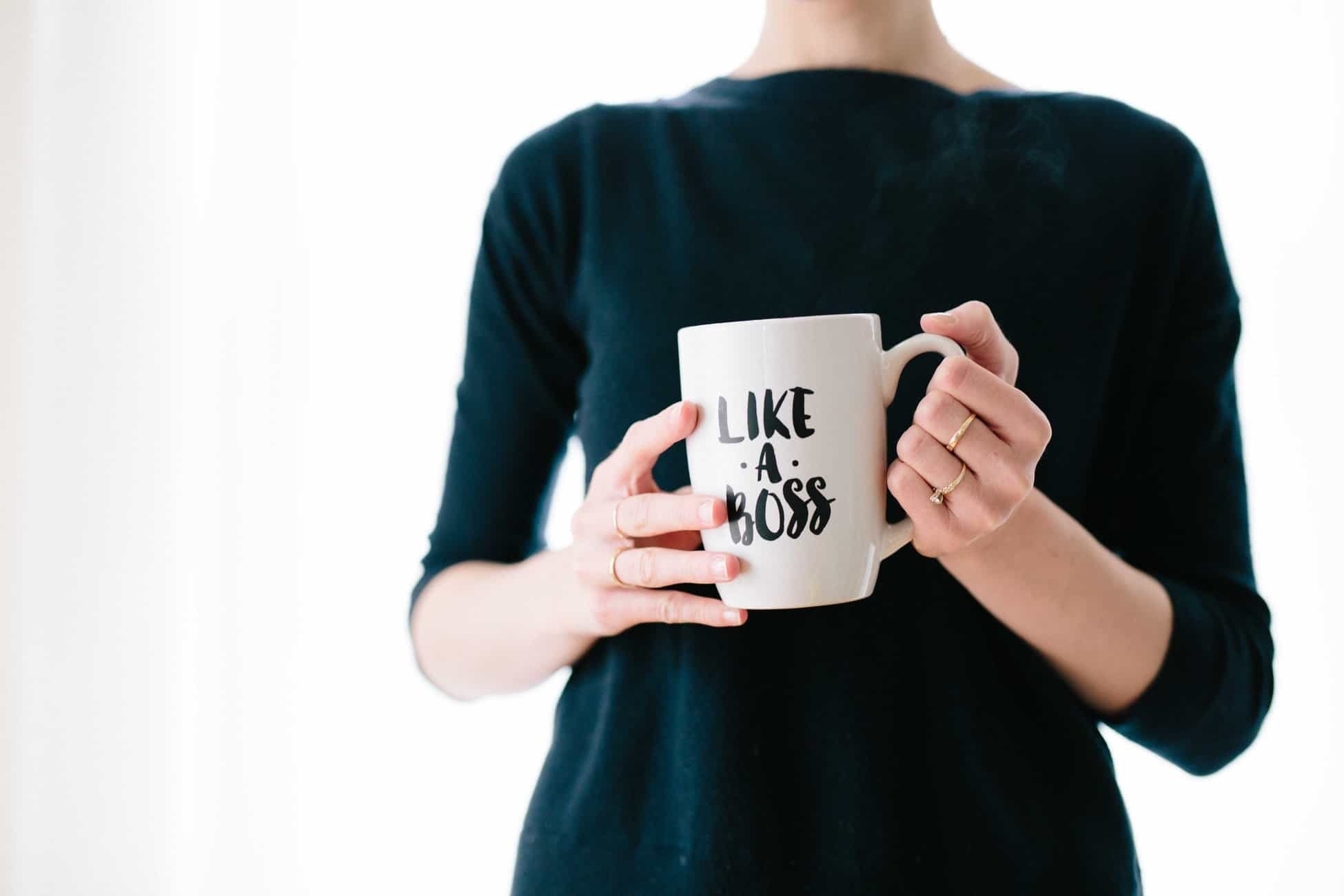 Woman in dark top holding a white mug printed with Like A Boss, illustrating productivity mindset