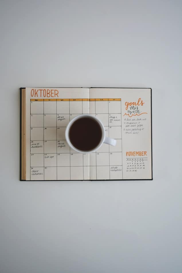 Coffee mug resting on an open planner showing an October calendar with monthly goals section