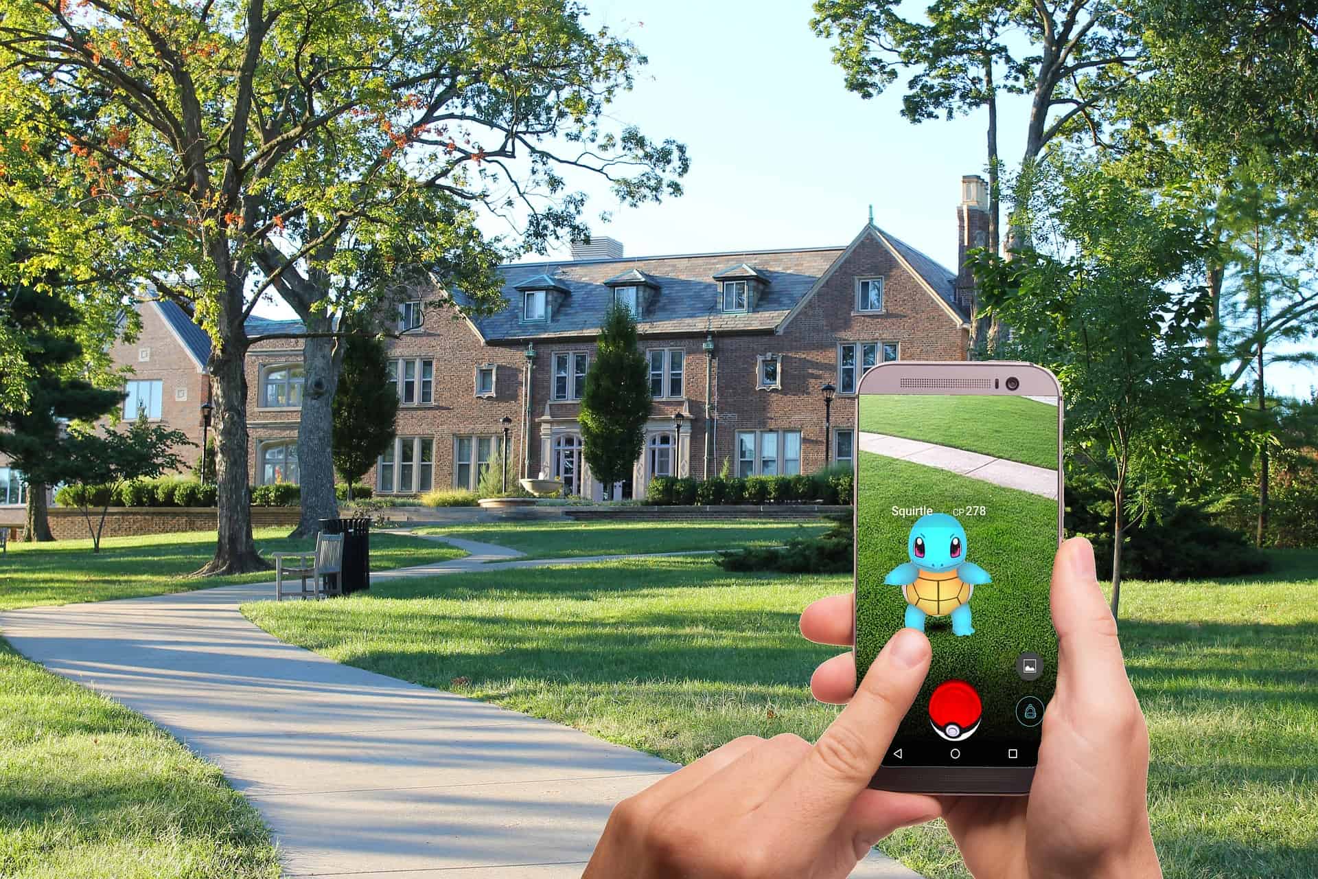 Hand holding a smartphone showing a Pokemon Go Squirtle overlaid on a real-world park and building