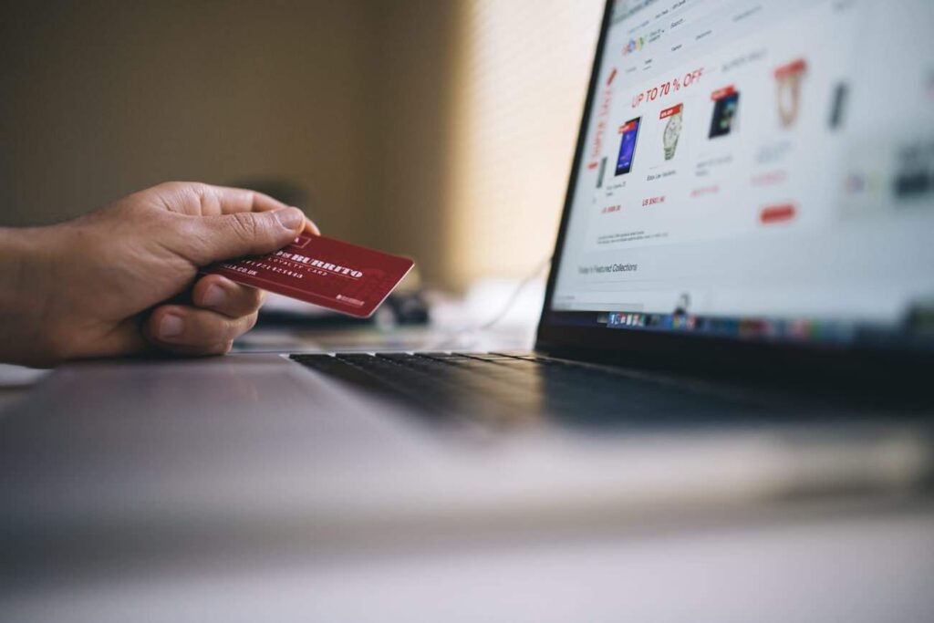 Person holding a credit card toward an open laptop showing an ecommerce store with discount offers