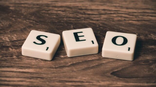 Three Scrabble tiles spelling SEO on a wooden surface, representing search engine optimisation concepts